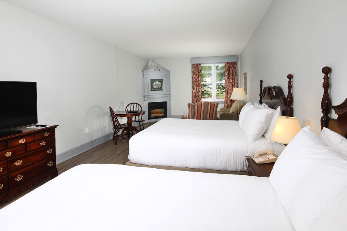 A hotel room with two beds, a television, a fireplace, and a dining area.