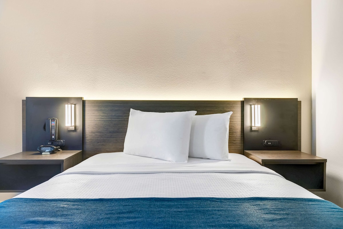 A hotel room with a neatly made bed, two bedside tables with lamps, and a modern headboard.