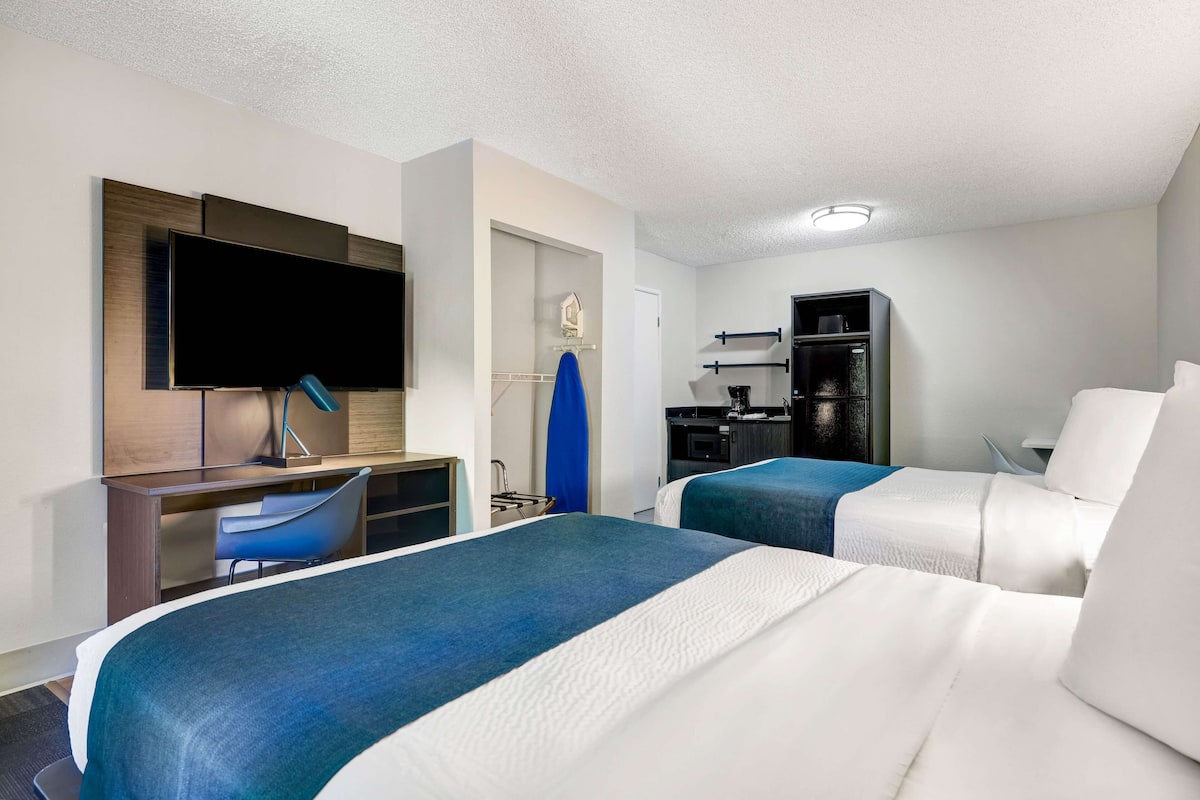 A hotel room with two beds, a desk, a TV, a mini-fridge, and a microwave.