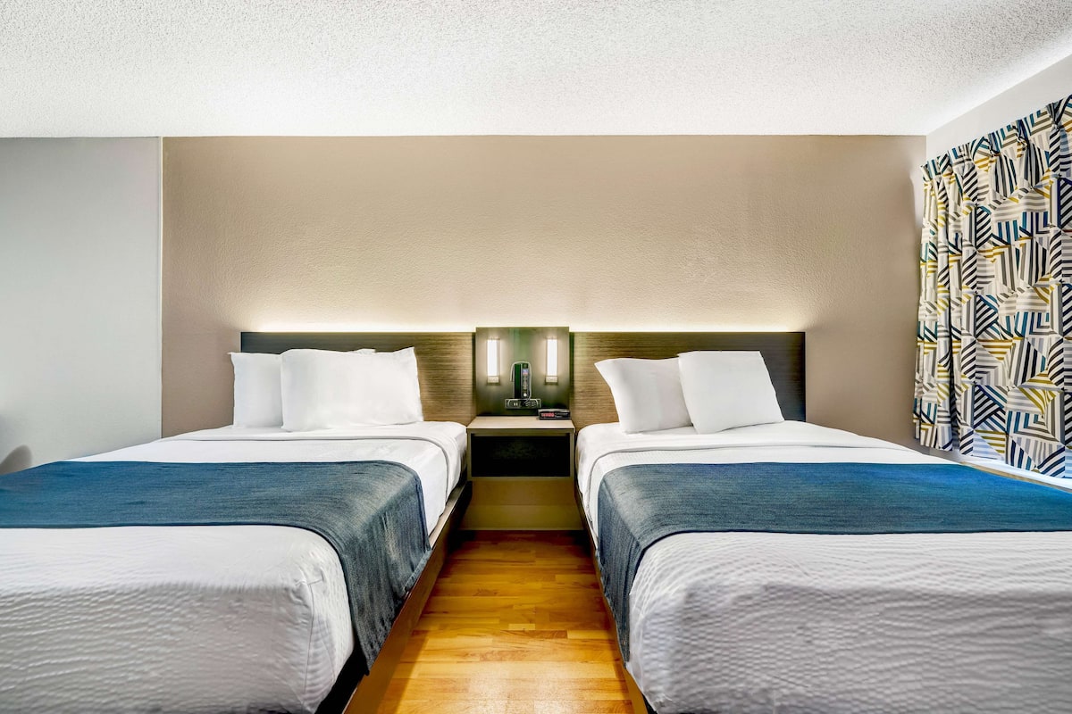 A hotel room with two beds, a nightstand with a lamp, and a patterned curtain.