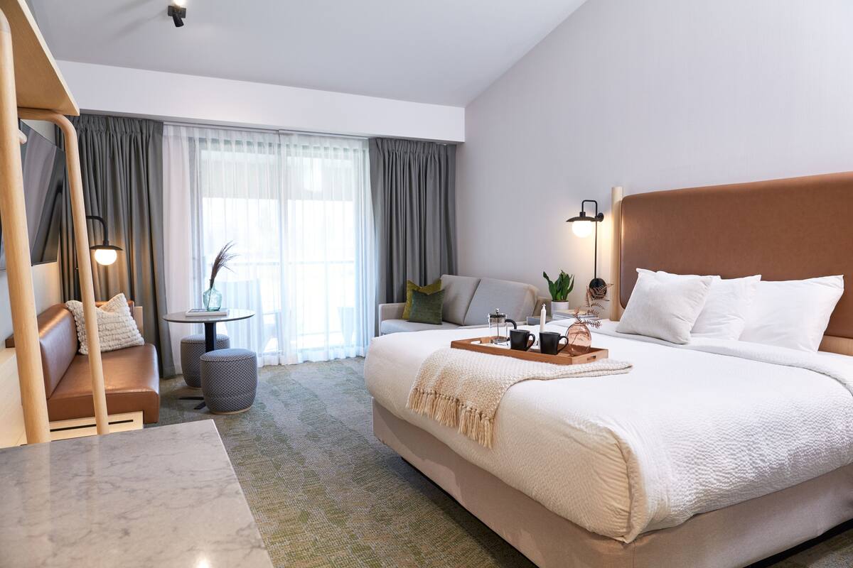 A modern hotel room with a large bed, a sofa, a small table, and a lamp.
