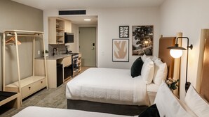 A compact hotel room with a kitchenette, a walk-in closet, and a bed with white bedding.