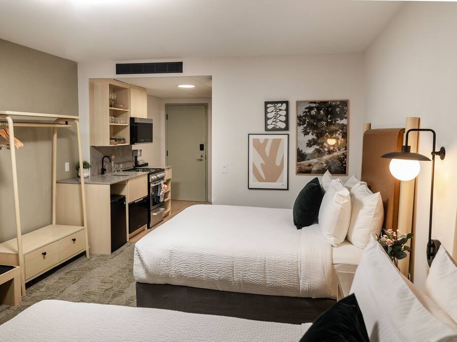A compact hotel room with a kitchenette, a walk-in closet, and a bed with white bedding.