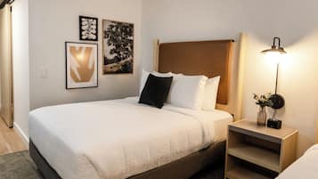 A neatly made bed with a white comforter and pillows, a bedside table with a lamp, and two framed artworks on the wall.