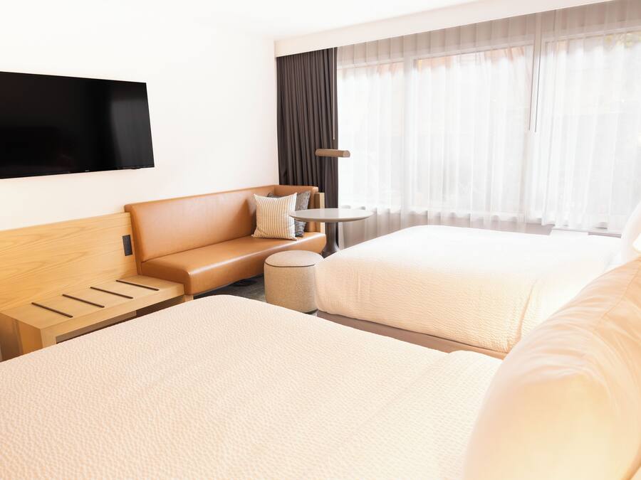 A hotel room with two beds, a sofa, a TV, and a window with curtains.