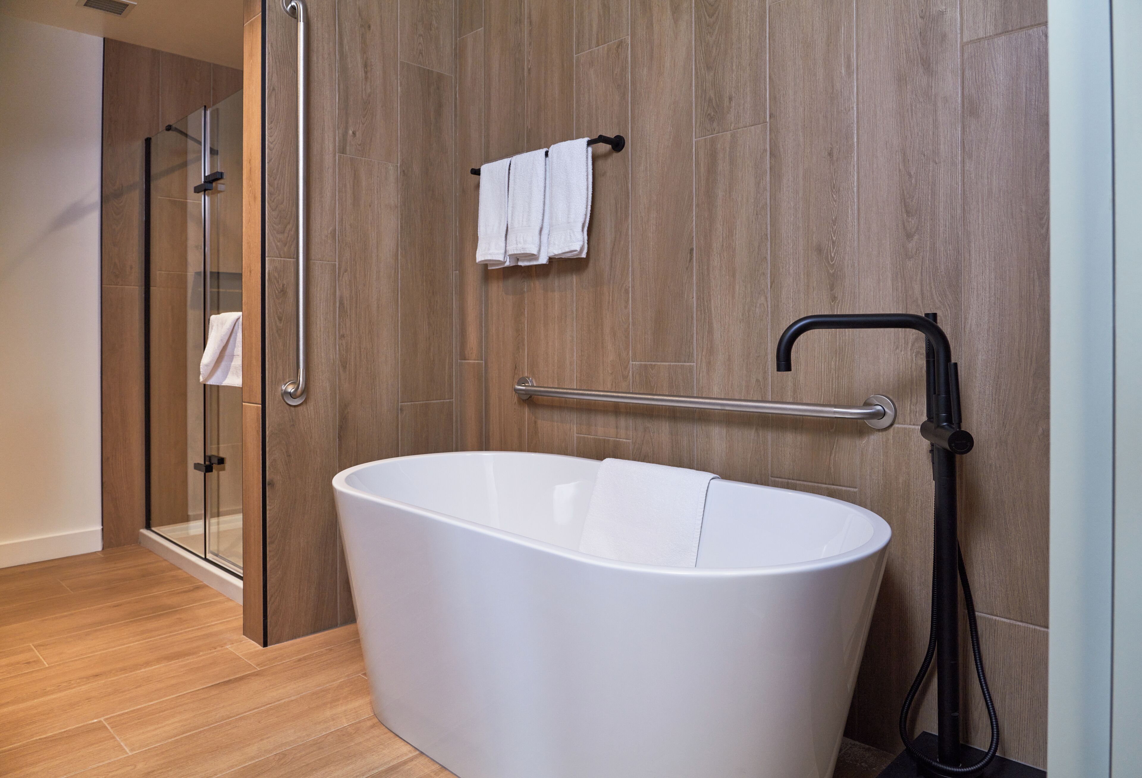 A modern bathroom with a freestanding bathtub, a glass shower enclosure, and a towel rack with two towels.