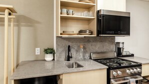 A modern kitchen with a built-in stove, microwave, and a shelf with glassware and dishes.