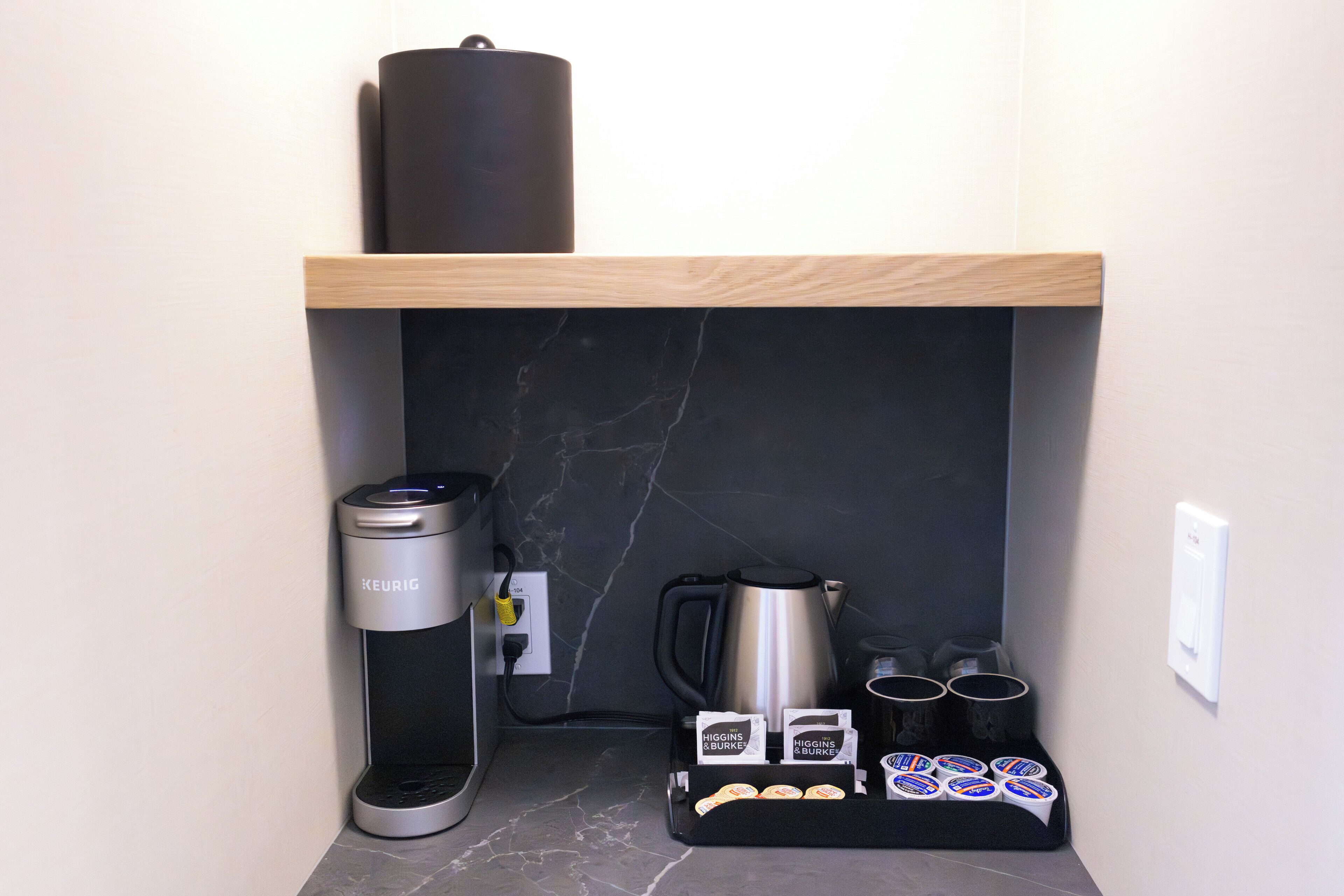 A compact kitchenette with a Keurig coffee maker, a coffee pot, and a coffee station with mugs and cups.