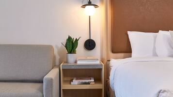 A neatly arranged hotel room with a bed, a bedside table with a lamp, a small plant, and a few books.