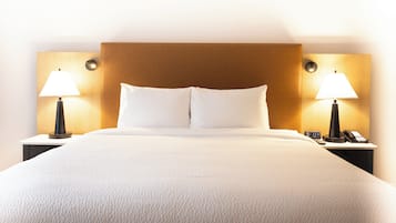 A hotel room with a large bed, two bedside lamps, a nightstand with a phone, and a wooden headboard.