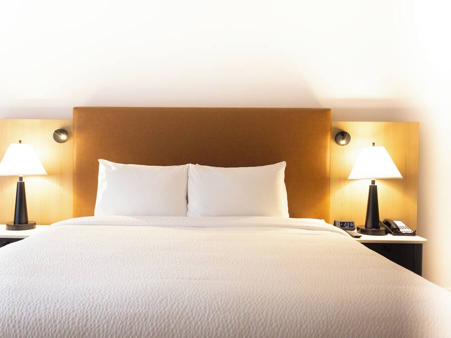 A hotel room with a large bed, two bedside lamps, a nightstand with a phone, and a wooden headboard.