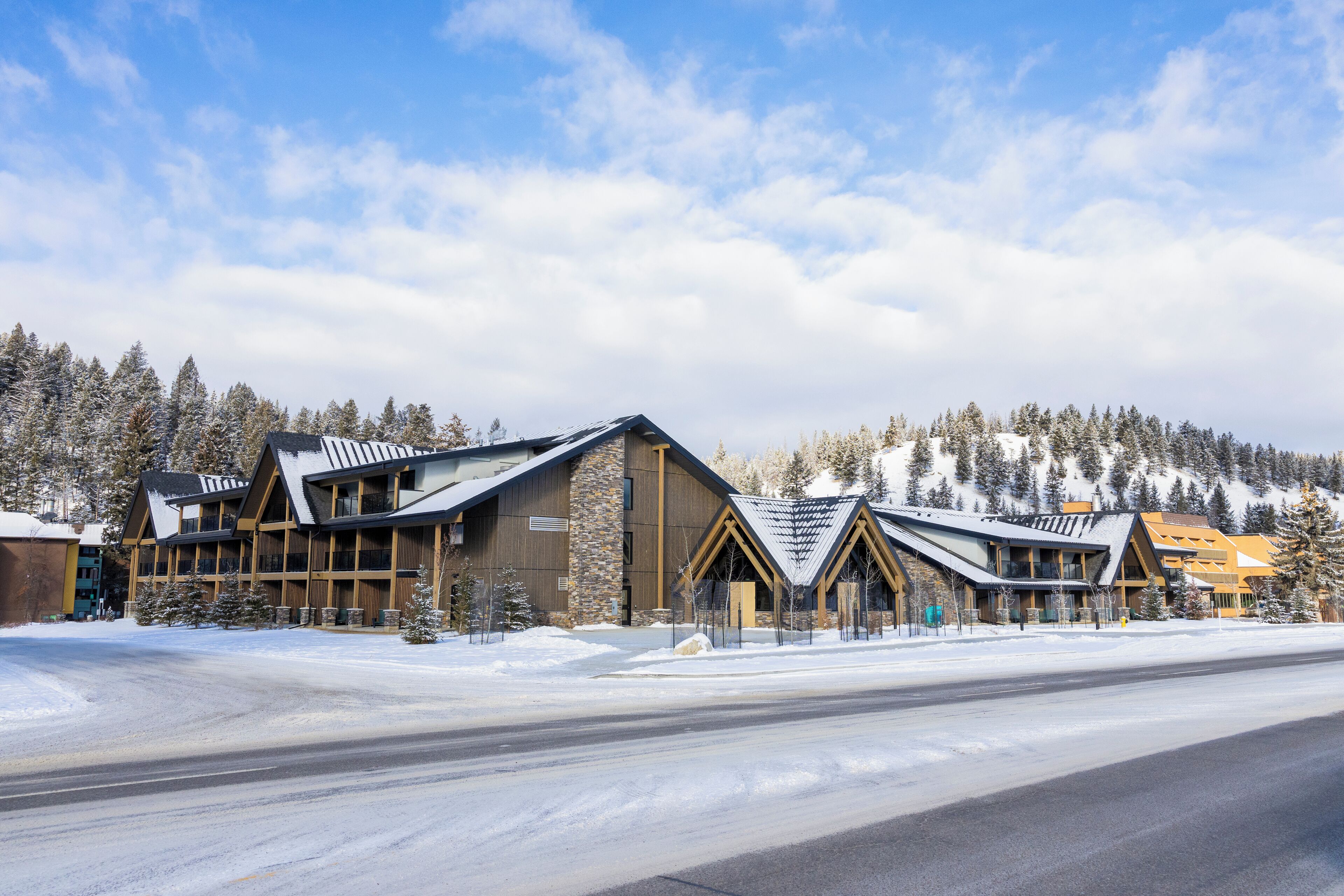 A modern lodge with a symmetrical design, featuring a central entrance flanked by two wings, set against a snowy backdrop with a clear sky.