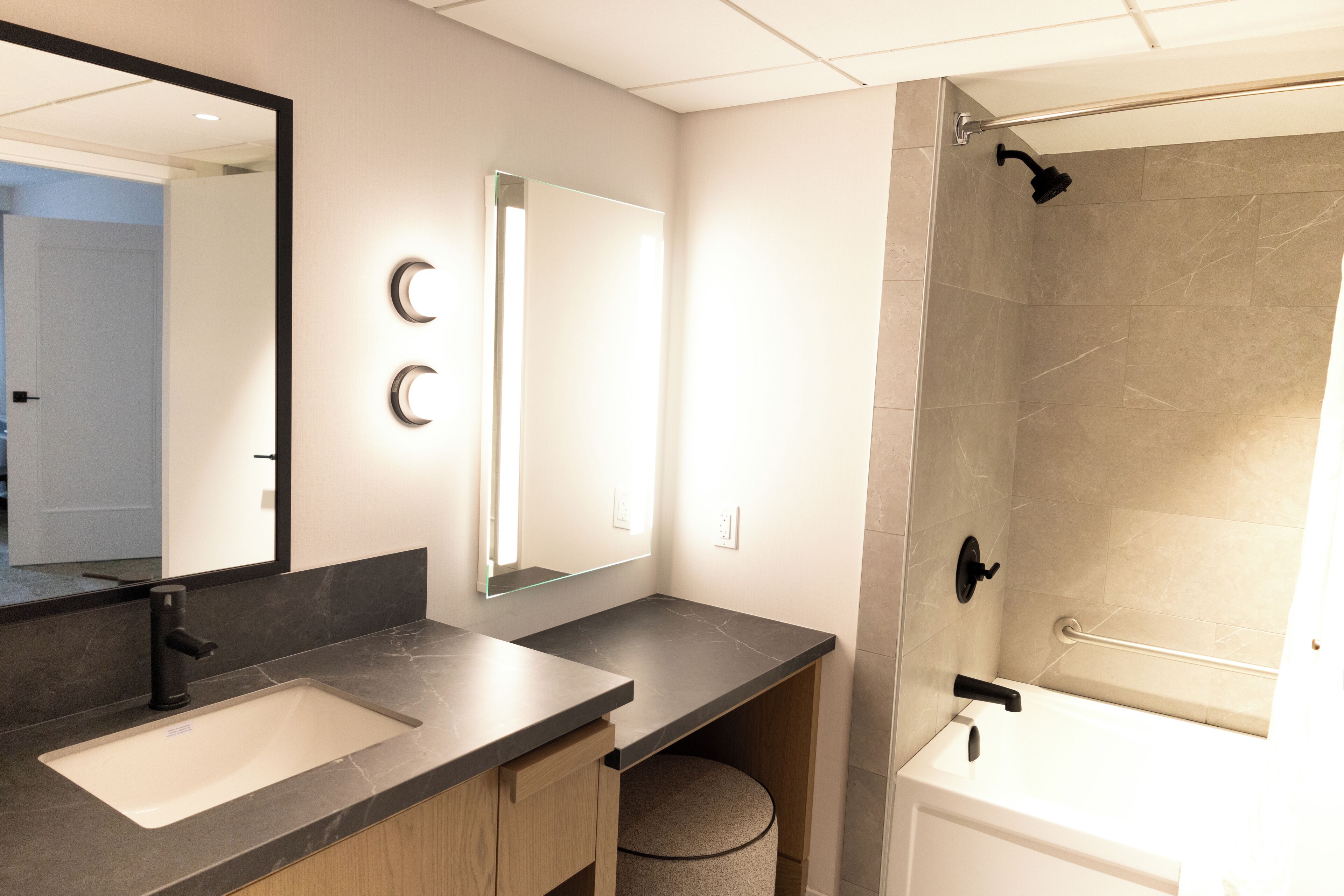 A modern bathroom with a double sink, a large mirror, a shower with a handheld showerhead, and a towel rack.
