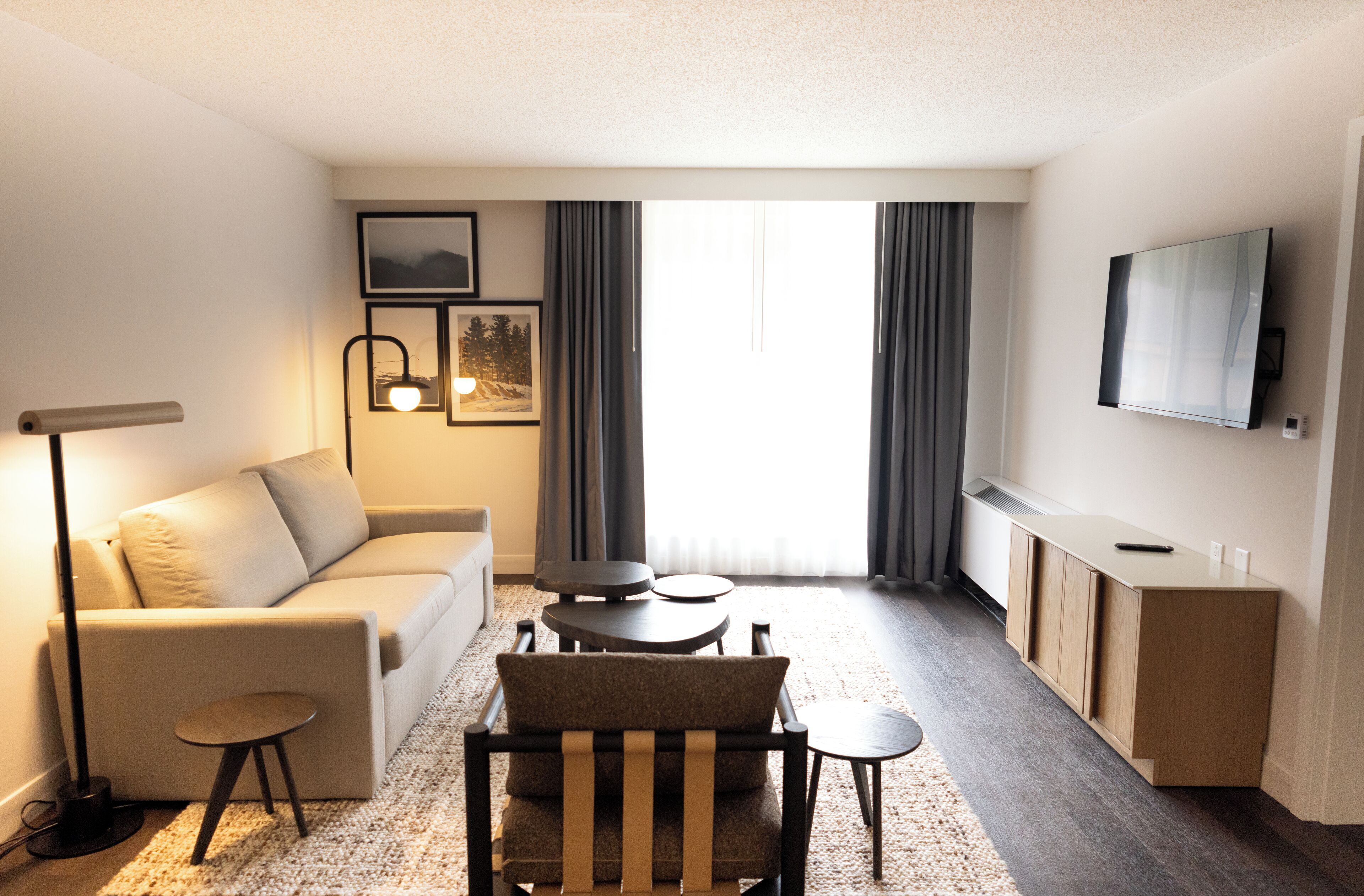 Ein modernes Hotelzimmer mit einer Couch, einem kleinen runden Tisch, einem Sessel, einem Schreibtisch und einem Flachbildfernseher an der Wand.