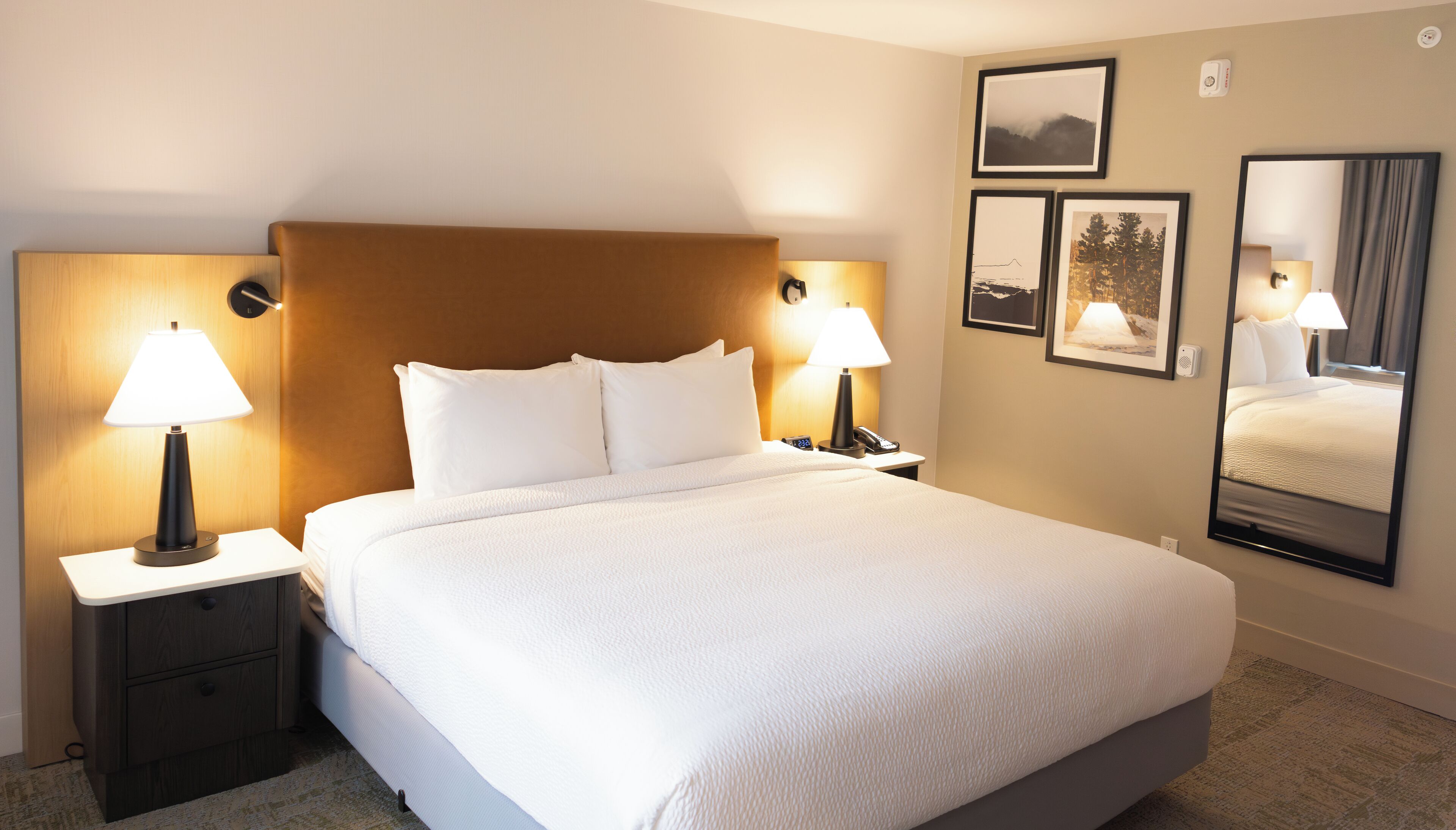 Une chambre d’hôtel avec un grand lit, deux tables de chevet avec des lampes, une table de nuit et un miroir fixé au mur.