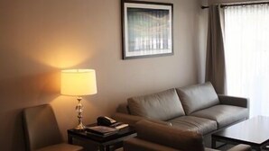 Una camera d'albergo con un divano, una sedia, un tavolino, una lampada e un quadro appeso al muro.