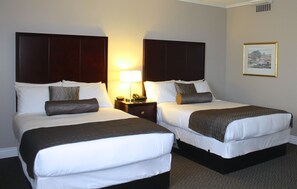 A hotel room with two beds, a nightstand, a lamp, and a framed picture on the wall. - Capital CityCenter Hotel (Victoria)