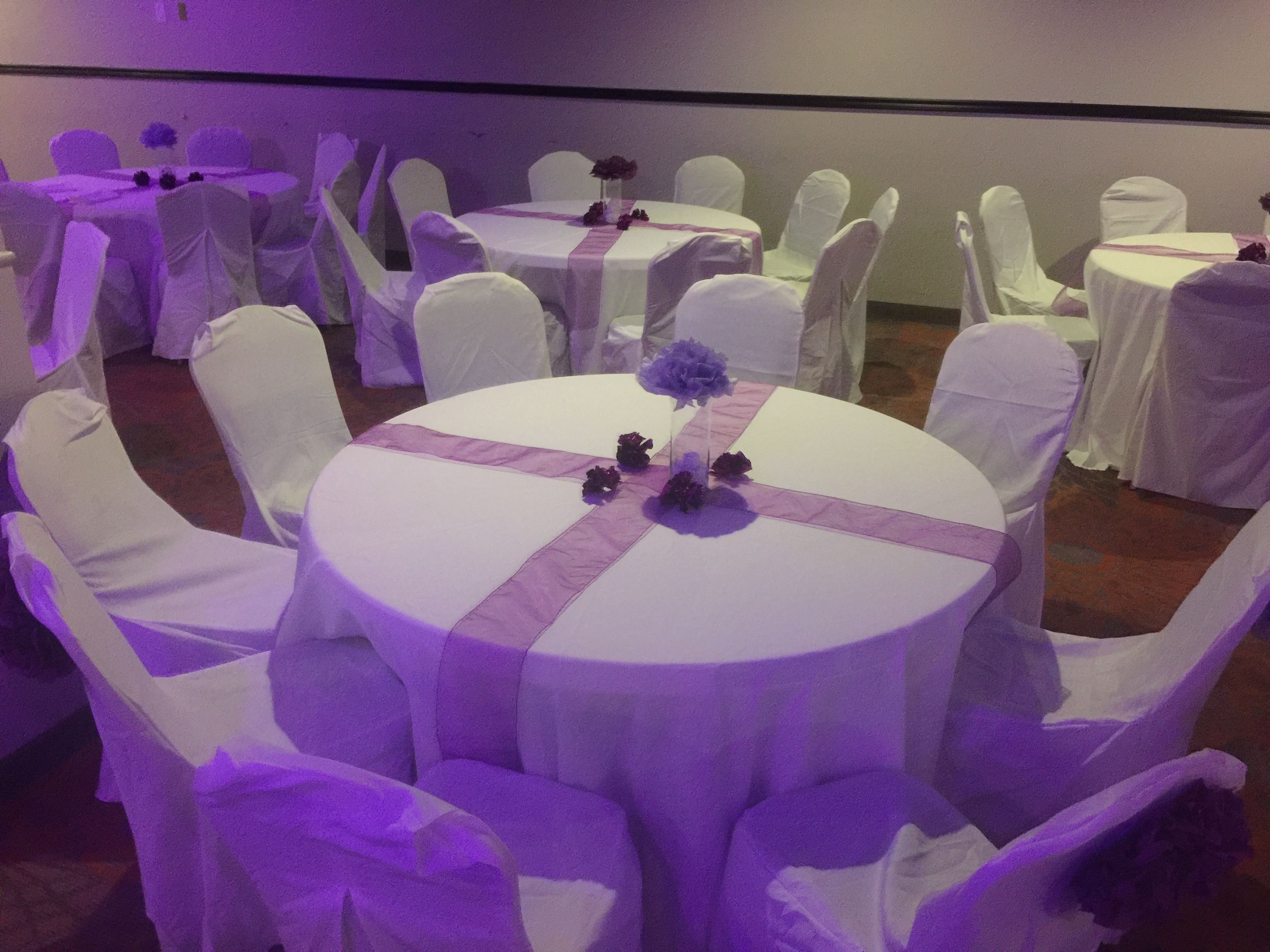 A banquet hall with round tables covered in white tablecloths and chairs with white covers.