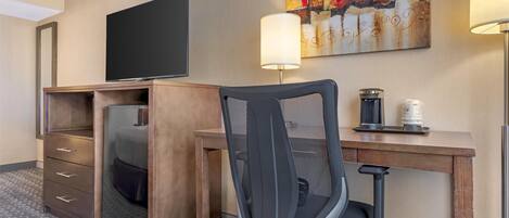 A hotel room with a wooden desk, a chair, a television, a lamp, and a coffee maker.
