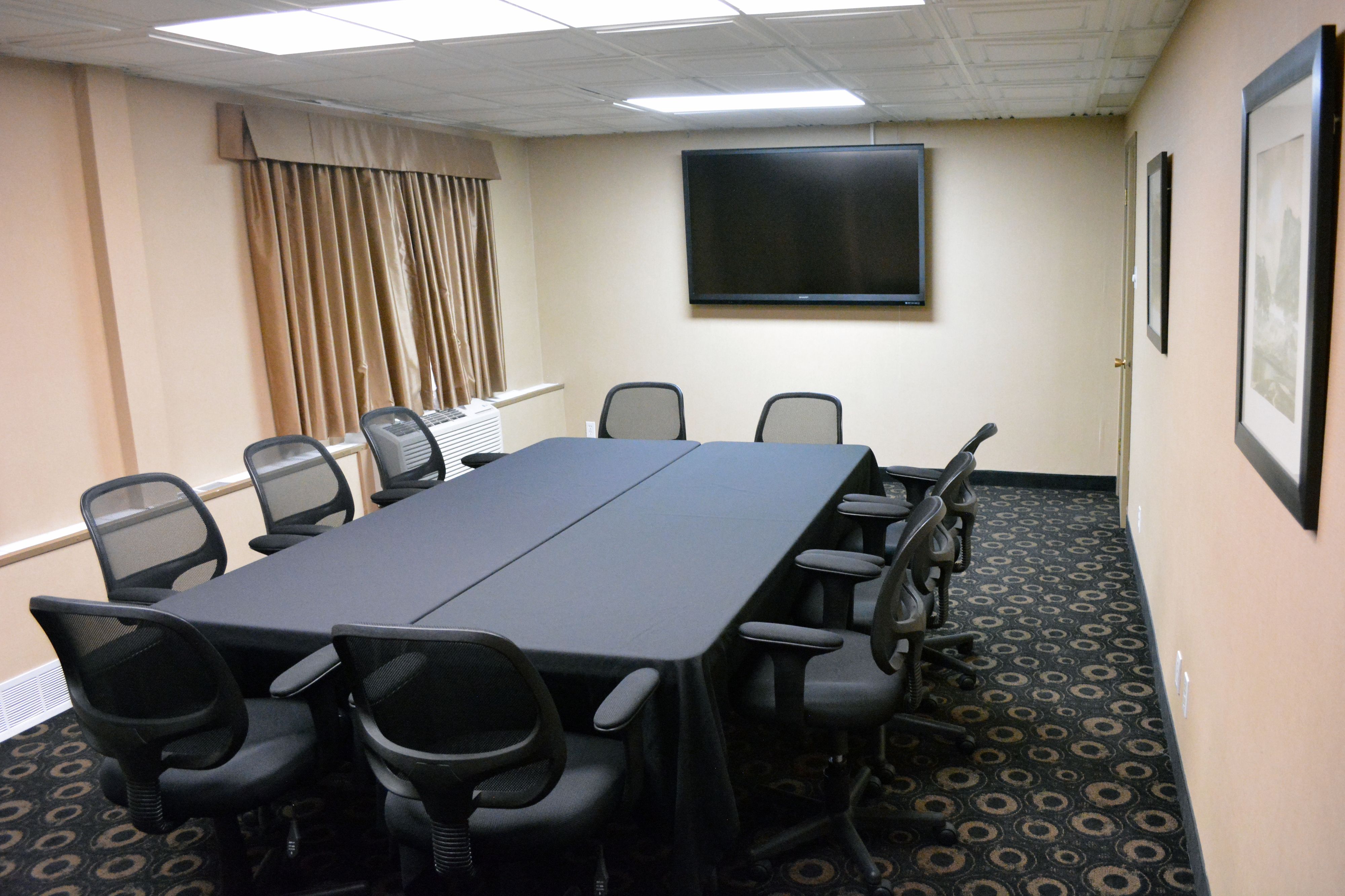 A conference room with a long table, chairs, a projector screen, and framed pictures on the wall.