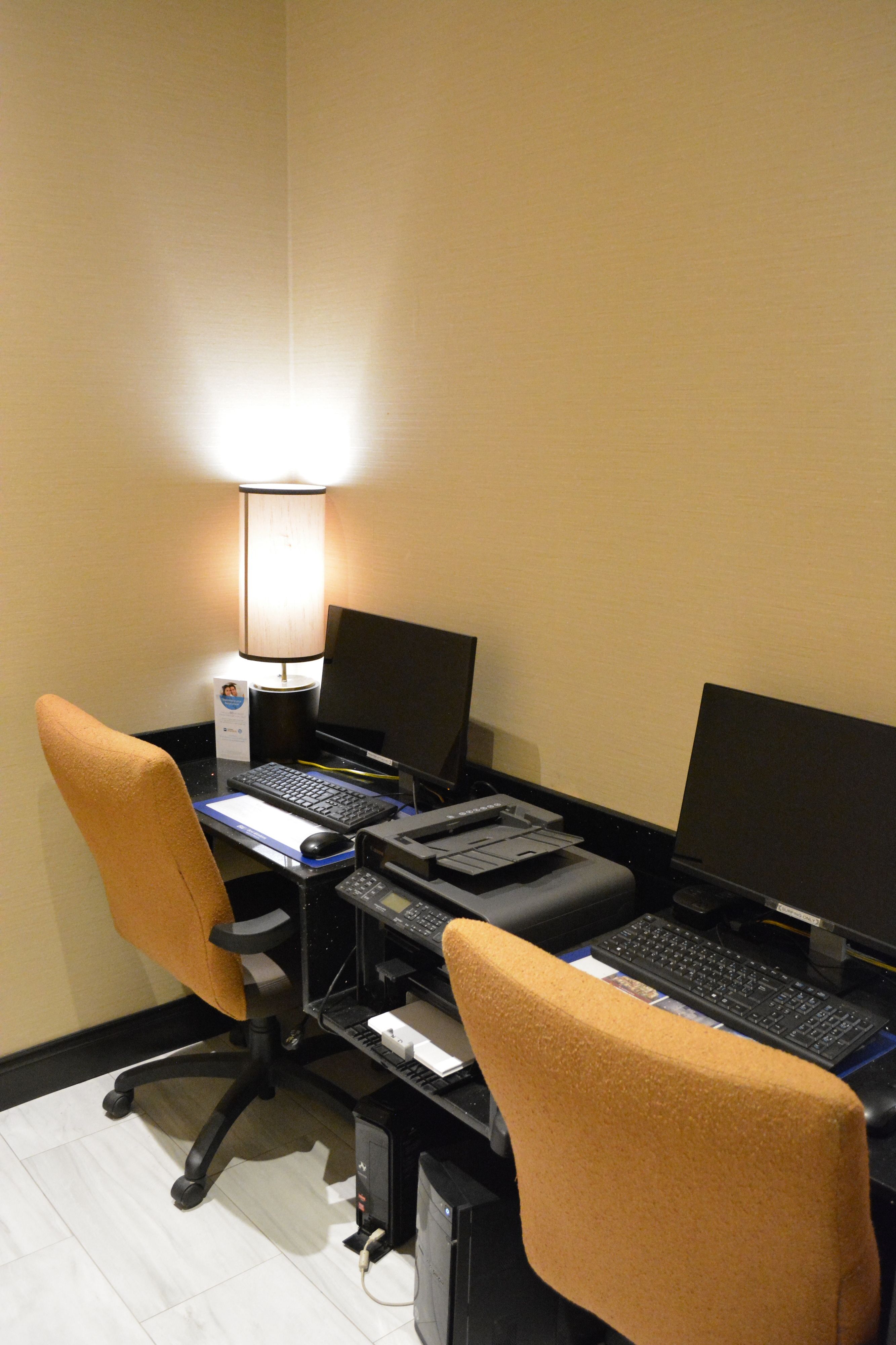 A hotel room with a desk setup including two computers, a lamp, and two office chairs.