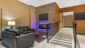 A hotel lobby with a seating area, a flat-screen TV mounted on a textured wall, and a striped carpet leading to a staircase. - Best Western Terrace Inn (Terrace)