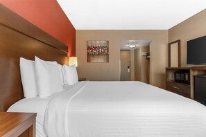 A hotel room with a large bed, a TV, a painting on the wall, and a door leading to a bathroom.