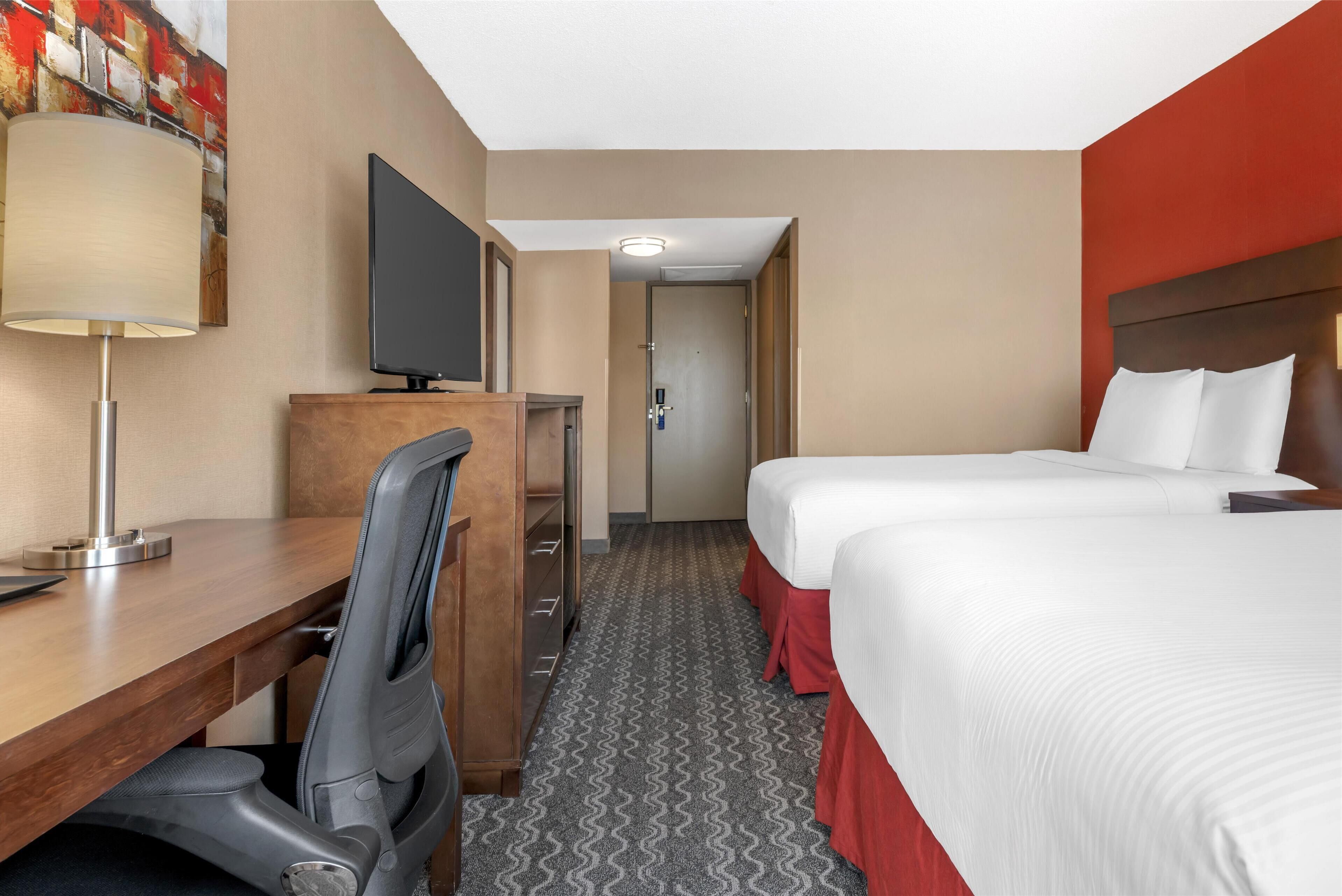 Habitación de hotel con escritorio, silla, dos camas, televisor y puerta que da a otra habitación.