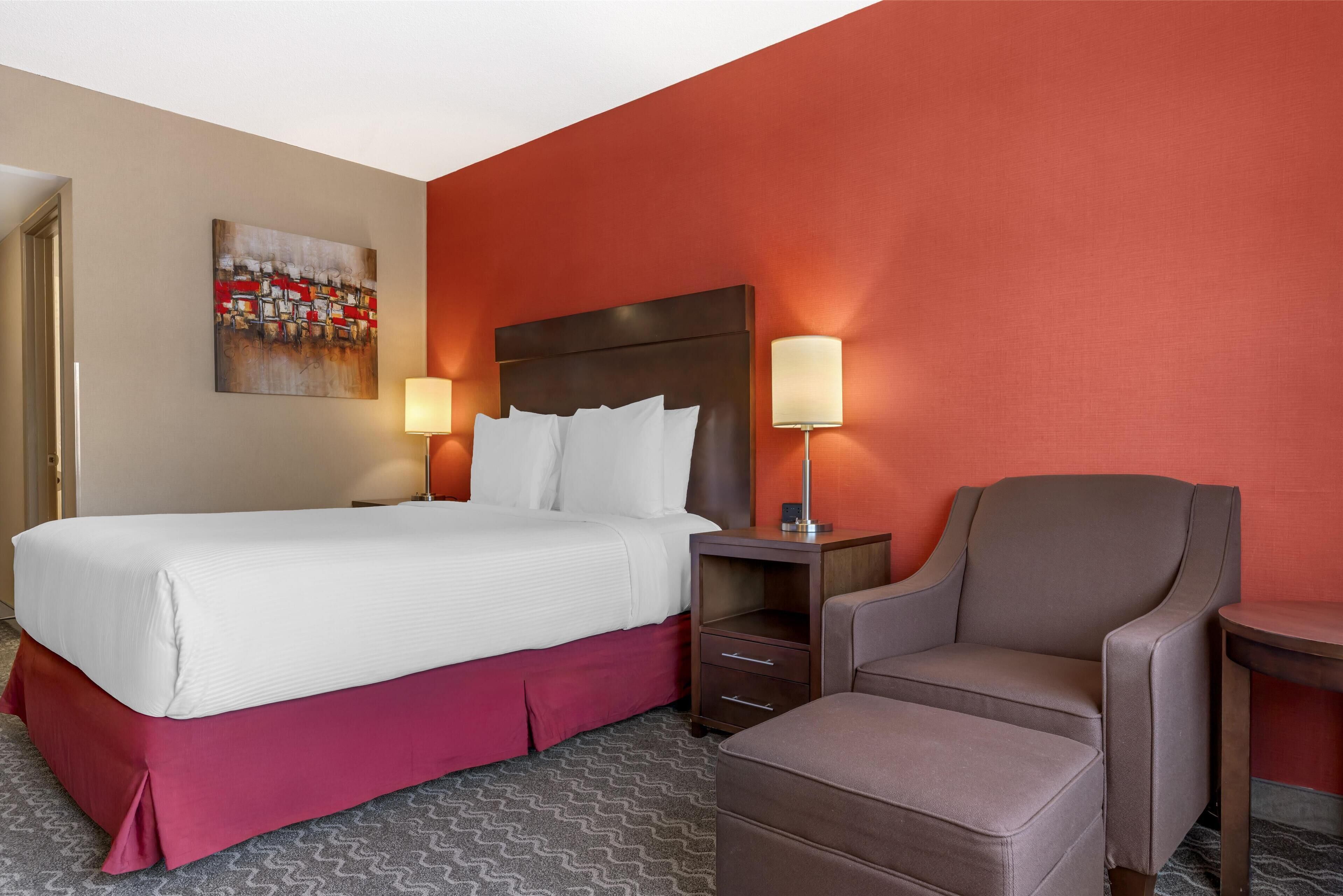 Una habitación de hotel con cama, una silla, una mesita de noche y una lámpara.
