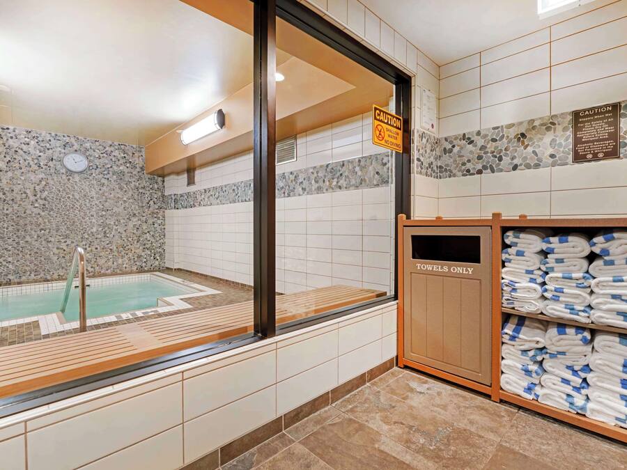 Zona de spa con bañera de hidromasaje, un cartel de precaución y toallas en estantes.