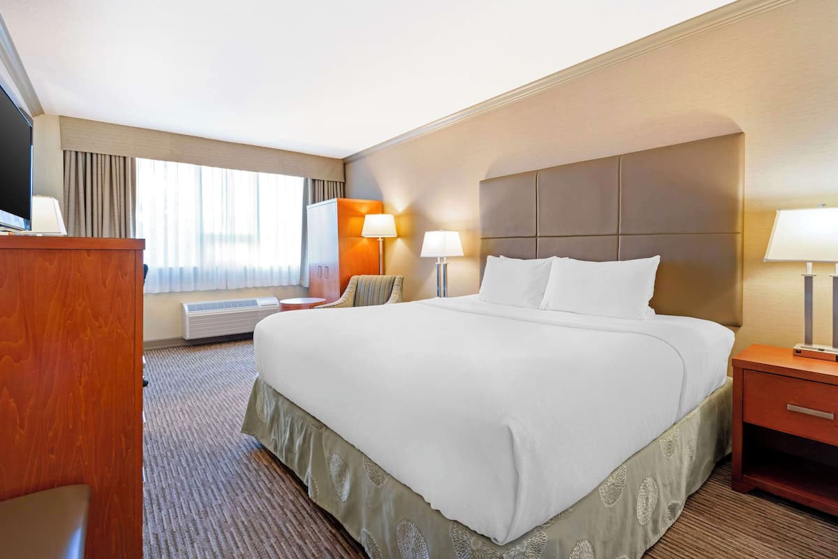 A hotel room with a large bed, bedside lamps, a desk with a flat-screen TV, and a window with curtains.