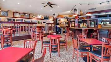 Een restaurant met houten tafels en stoelen, een bar en een plafondventilator.