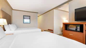 Una habitación de hotel con dos camas, un televisor, un microondas y una mesita con una lámpara.
