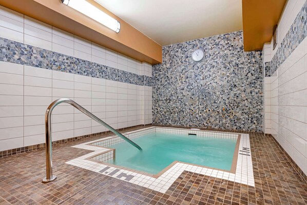 A swimming pool with a tiled floor and walls, a metal ladder, and a clock on the wall.