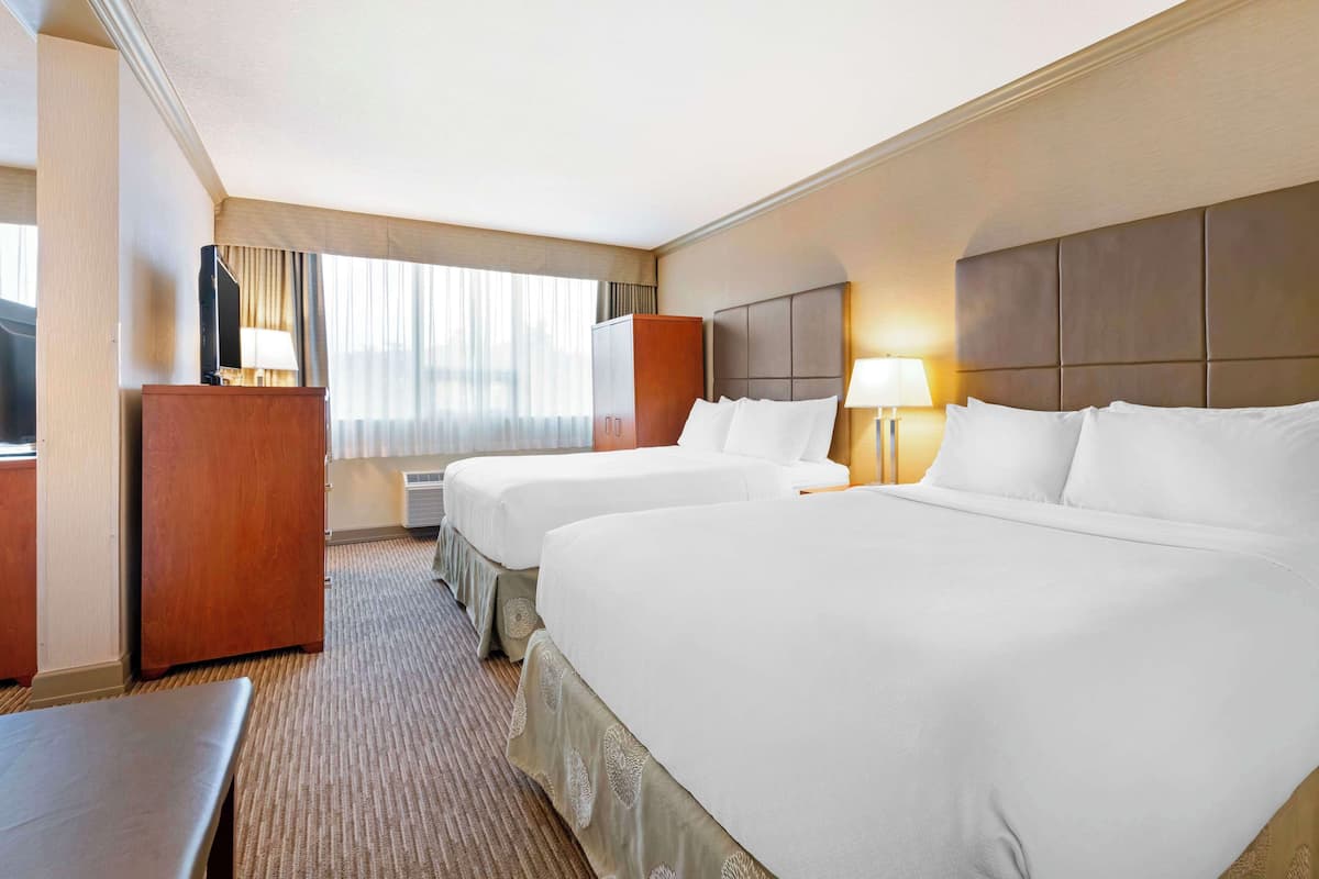 A hotel room with two beds, a desk, a wardrobe, and a large window with curtains.