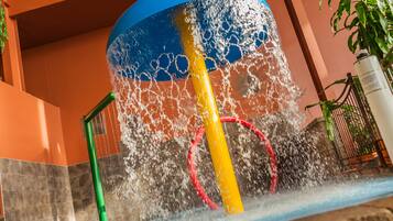 A water feature with a yellow and red structure, surrounded by a tiled wall and a potted plant.
