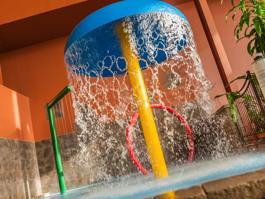 A water feature with a yellow and red structure, surrounded by a tiled wall and a potted plant.