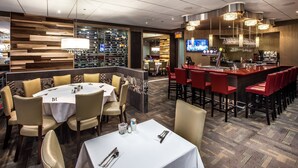 A restaurant with round tables and red bar stools, a wine rack, and a TV screen. - Ambassadeur Hotel (Québec City)