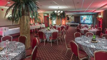 A banquet hall with round tables, red chairs, and zebra-striped tablecloths.