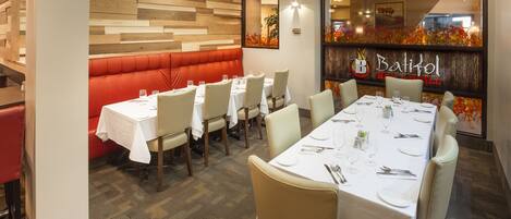 A restaurant interior with a long dining table, cushioned booths, and a wall with a wooden panel design.