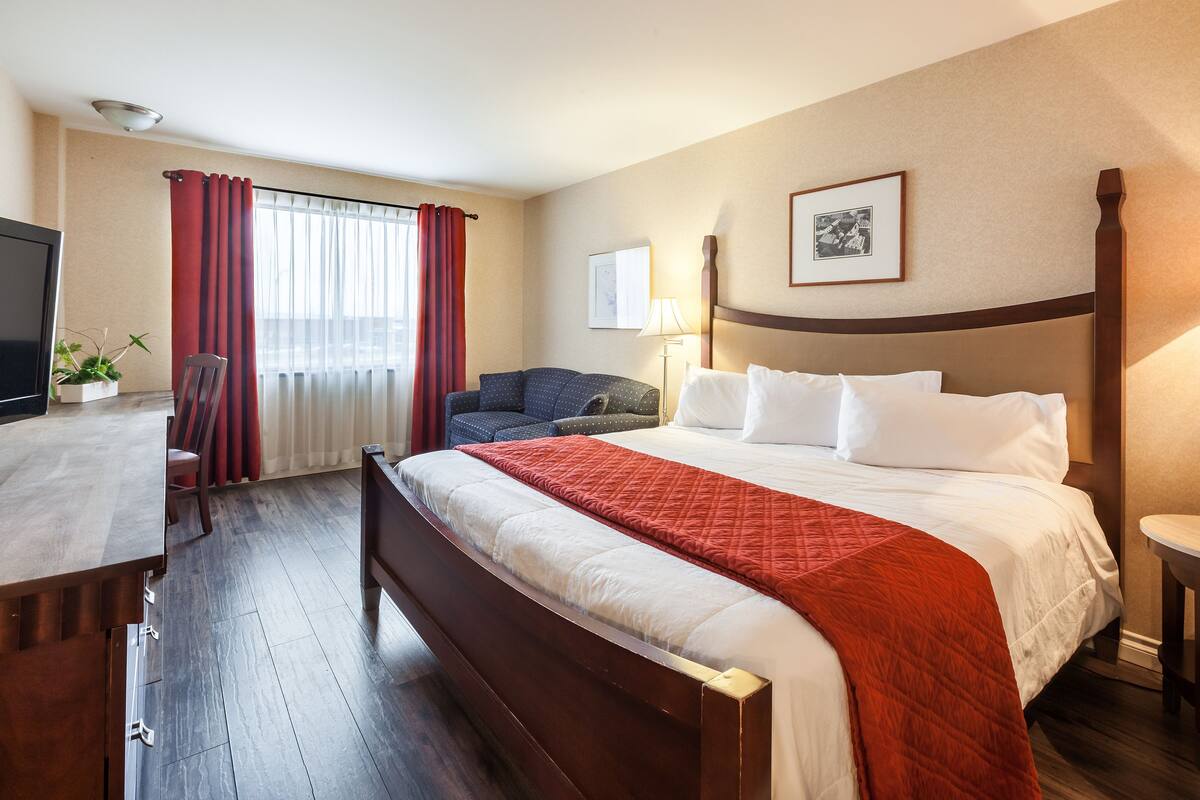 A hotel room with a large bed, a desk, a chair, a TV, and a window with curtains.