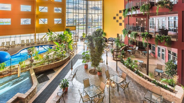 A spacious indoor atrium with a swimming pool, outdoor seating area, and multiple balconies with plants. - Ambassadeur Hotel (Québec City)