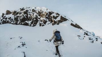 Una persona caminando por un sendero montañoso cubierto de nieve, cargando una mochila.