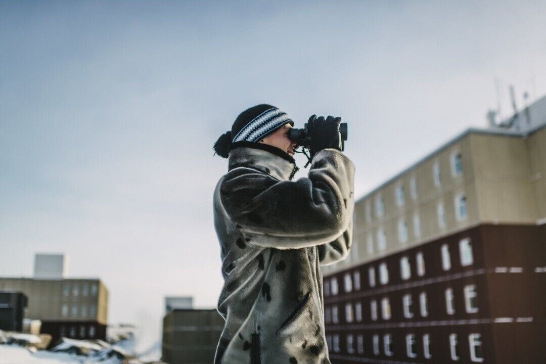 A person in a snowy environment, wearing a winter coat and gloves, holding a camera.
