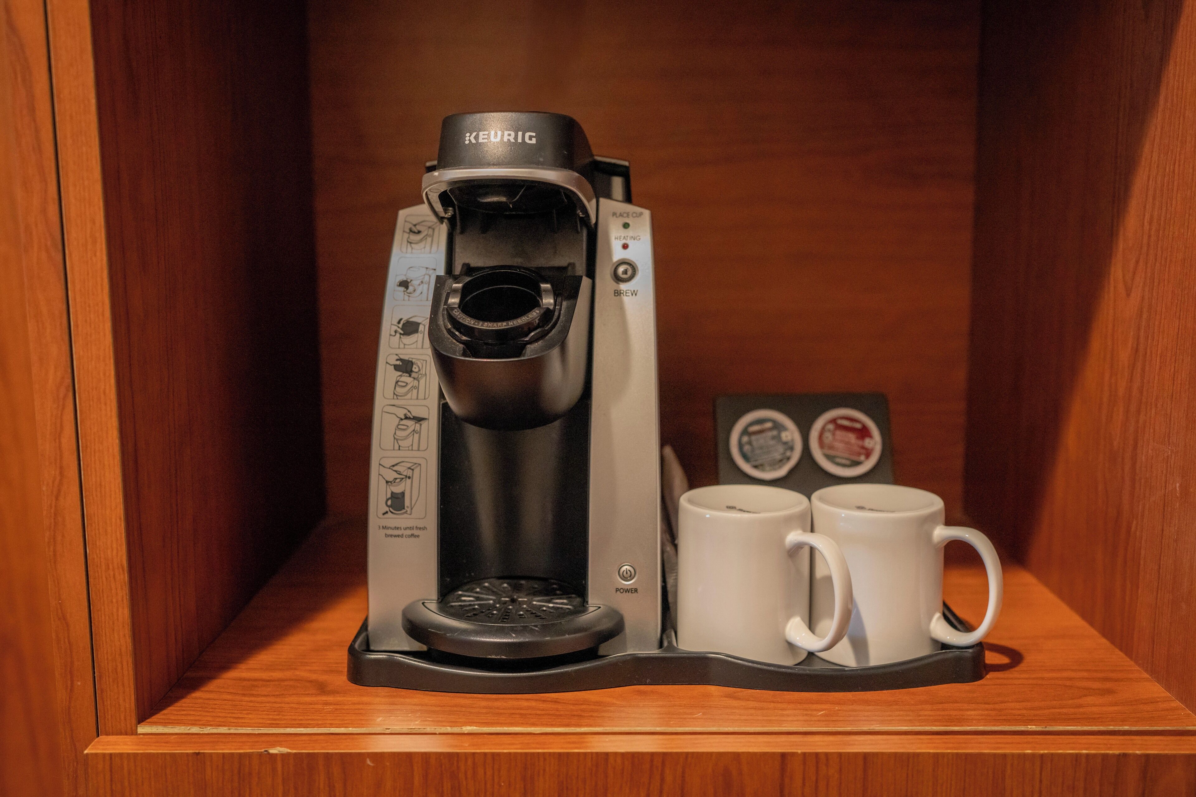Una cafetera Keurig con dos tazas blancas sobre una estantería de madera.