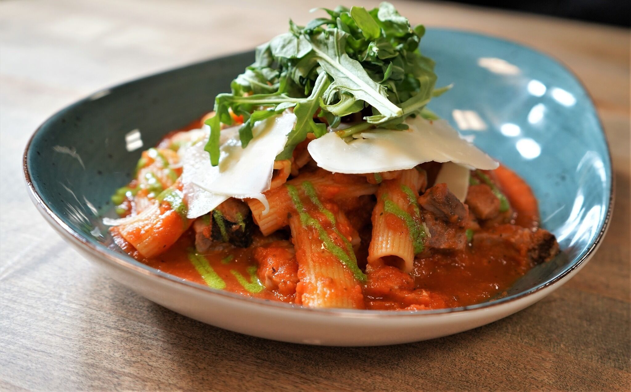 Un plato de pasta con salsa de tomate, adornado con vegetales verdes y queso rallado.