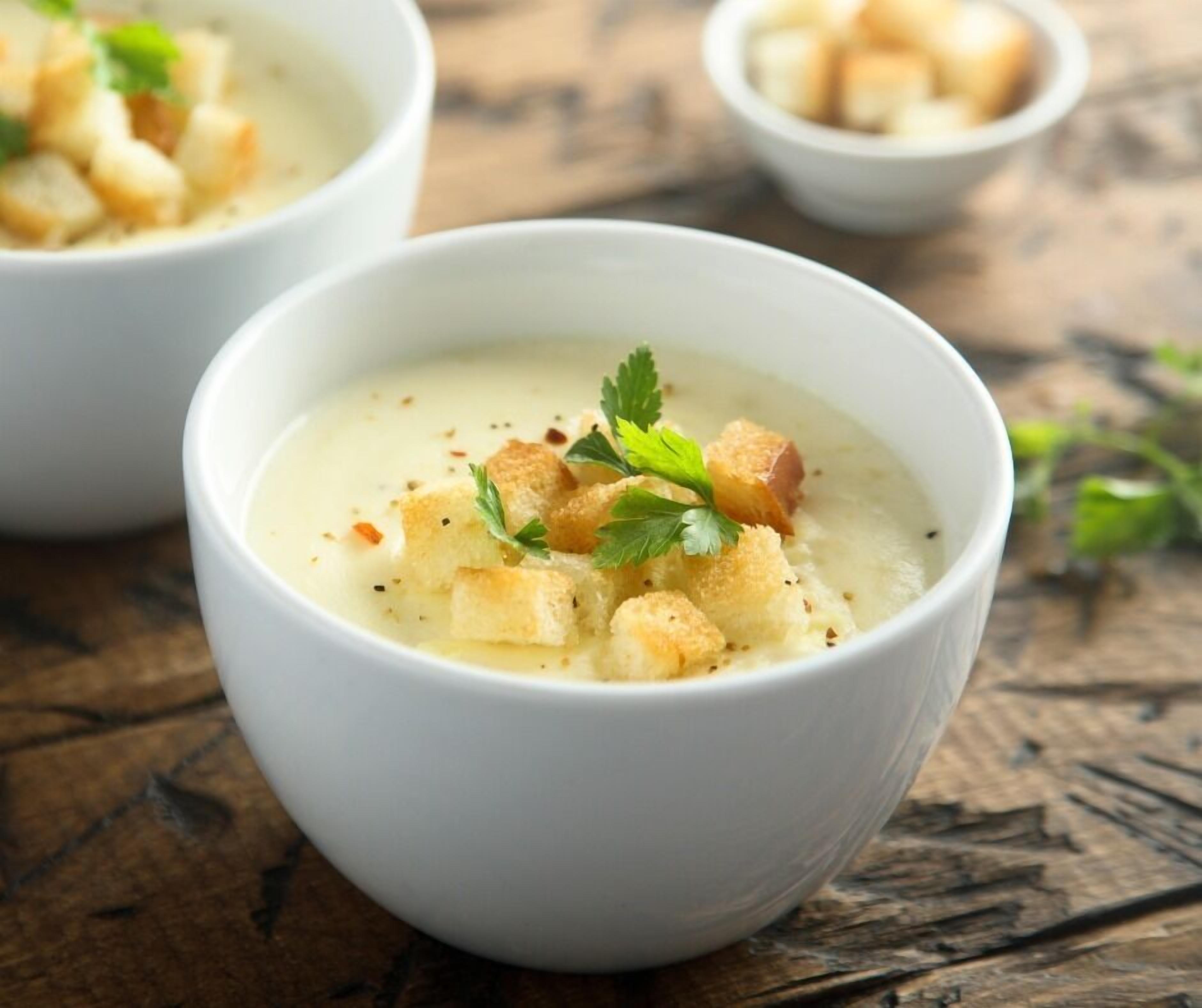 A bowl of soup garnished with croutons and parsley, served in a white bowl on a wooden surface.