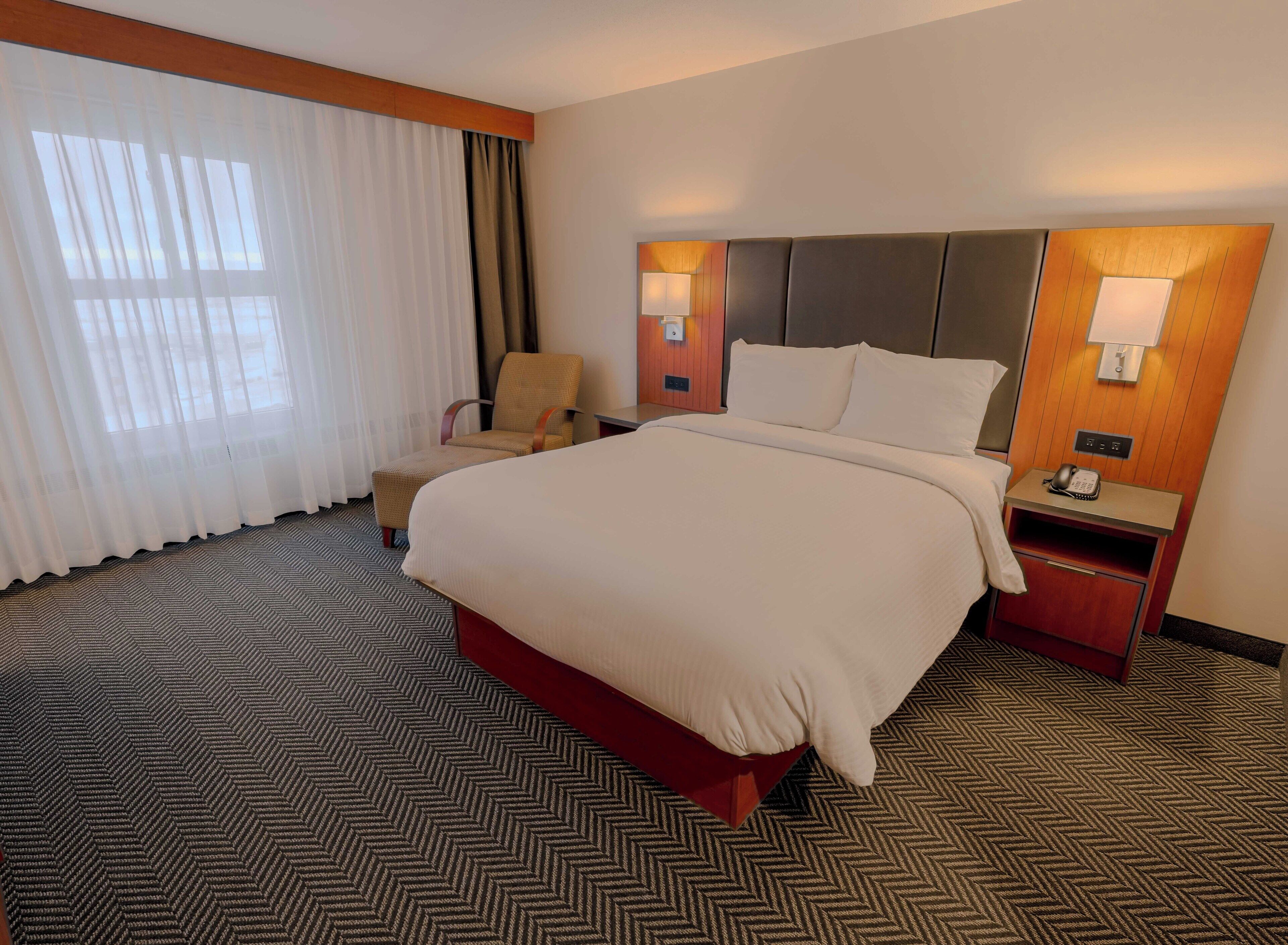 A hotel room with a large bed, a chair, a nightstand, and a lamp.