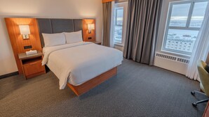 Ein Hotelzimmer mit einem großen Bett, zwei Nachttischen mit Lampen, Blick auf eine verschneite Landschaft durch das Fenster und einem Parkettboden mit Fischgrätmuster.