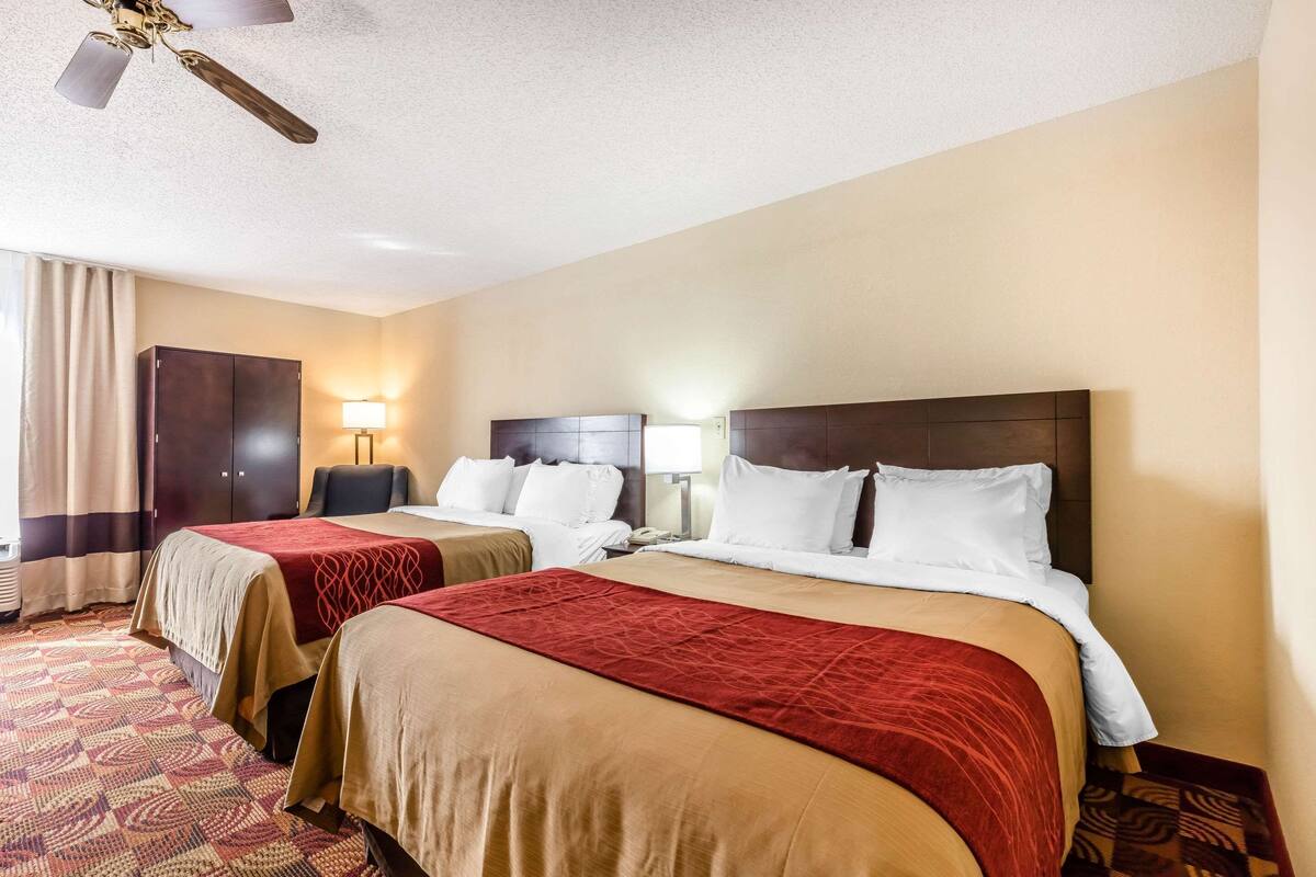A hotel room with two beds, a ceiling fan, a desk, and a lamp.